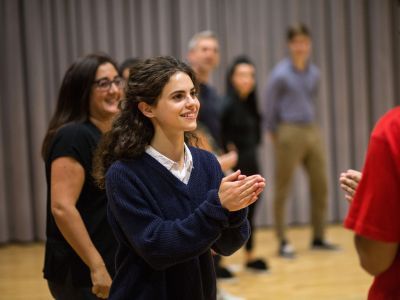A girl wearing a blue jumper holds her hands in front of her. She has a smile on her face.